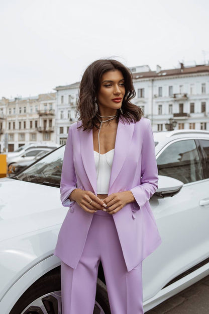 Woman in a lavender suit standing next to a white car on a city street.