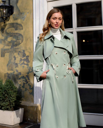 Woman wearing a light green trench coat standing outdoors.