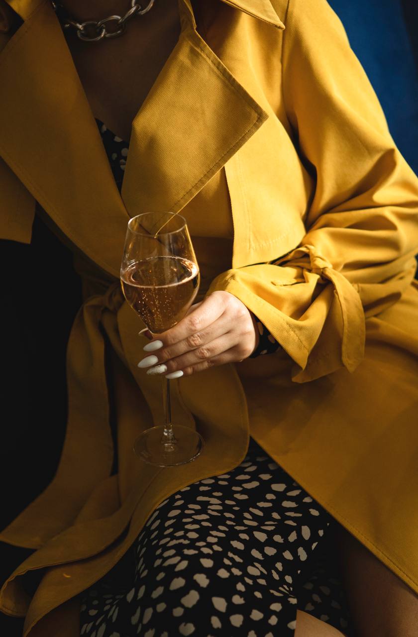 Person in a yellow coat holding a glass of champagne against a dark background