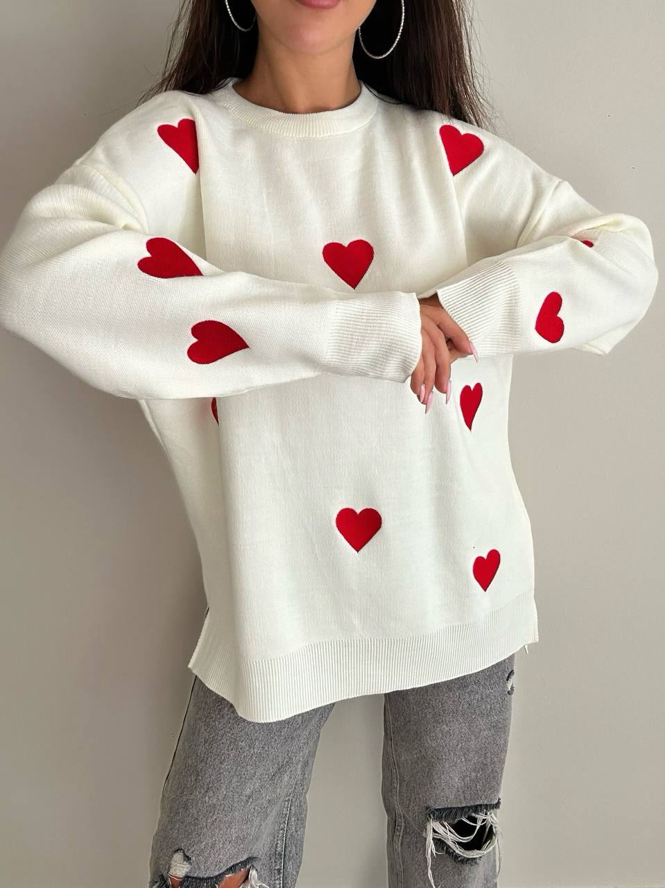 White sweater with red heart patterns worn by a person against a neutral background