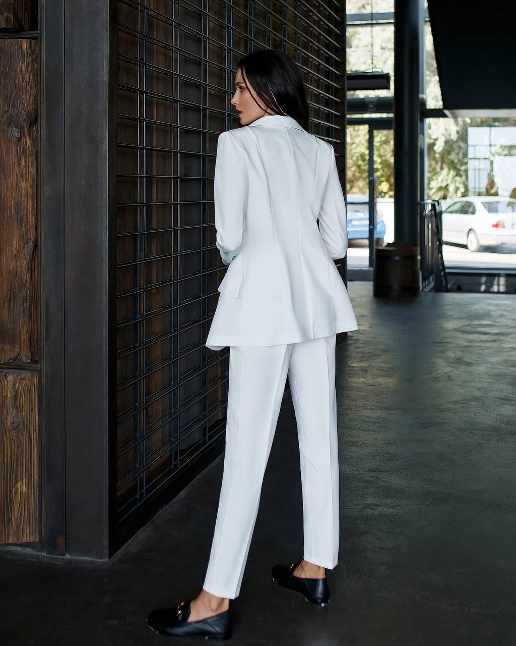 Woman in a white suit standing against a dark wall.