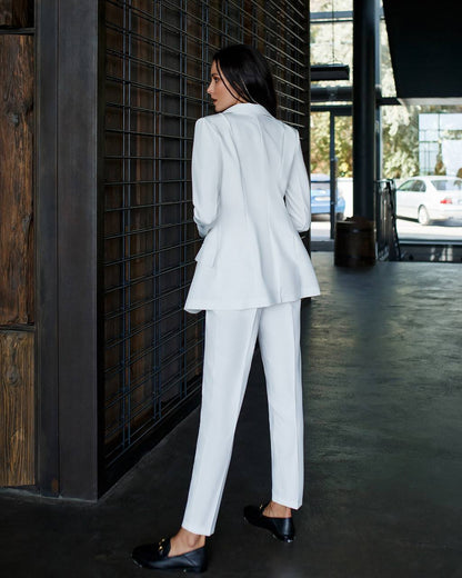 Woman in a white suit standing against a dark wall.