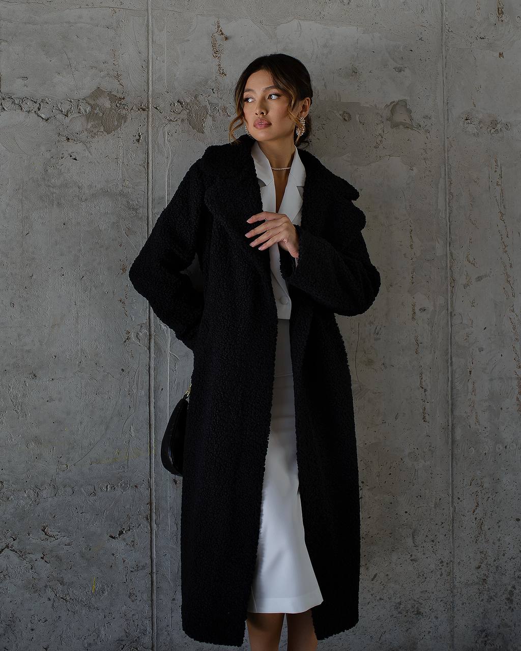 Woman wearing a black coat against a textured gray wall