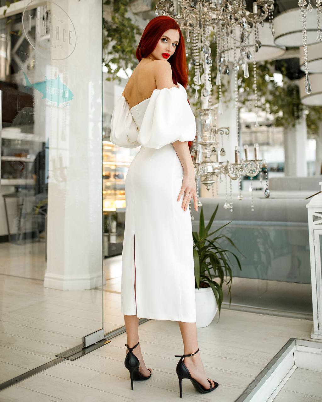 Woman in a white off-shoulder dress standing in an elegant indoor setting.
