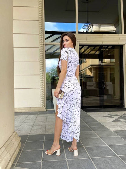 Woman in a white dress with black polka dots standing on a tiled floor.