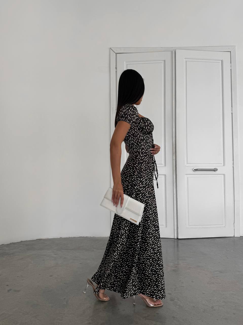 Woman in a black and white patterned dress holding a clutch in a minimalistic setting.