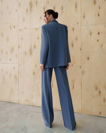 Person wearing a blue suit standing against a wooden wall.