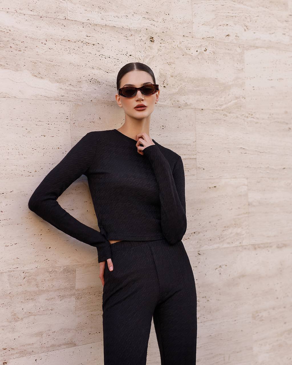 Person wearing a black outfit against a light stone wall