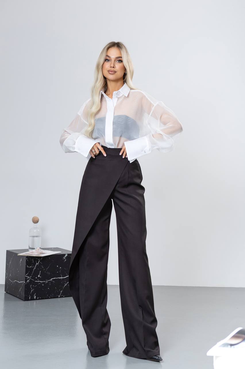Woman wearing a white blouse with sheer sleeves and black high-waisted pants on a white background