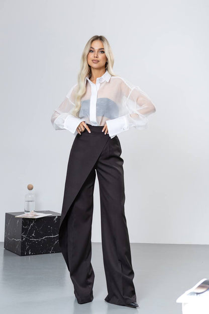 Woman wearing a white blouse with sheer sleeves and black high-waisted pants on a white background