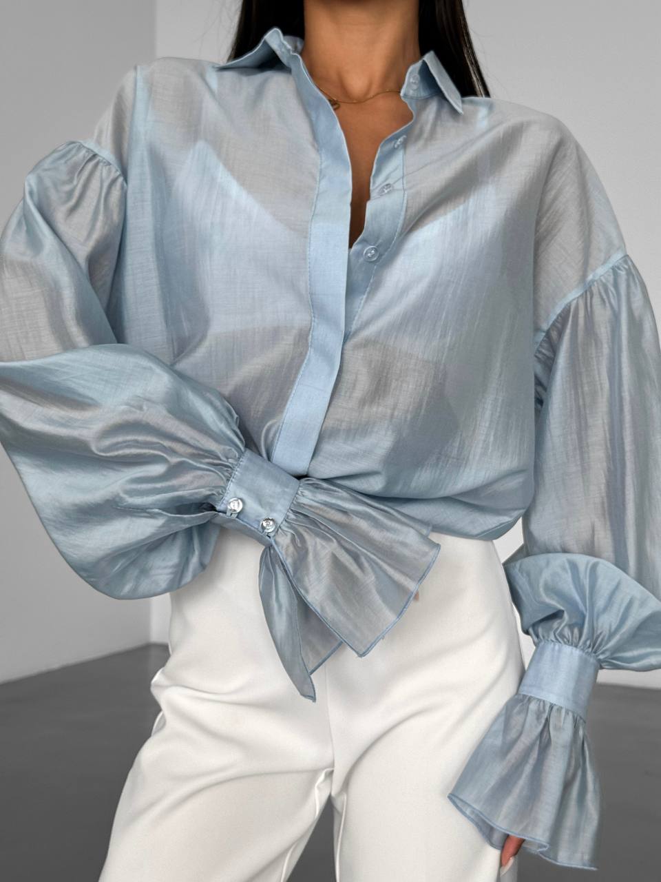 Light blue sheer blouse with ruffled sleeves worn over a white outfit.