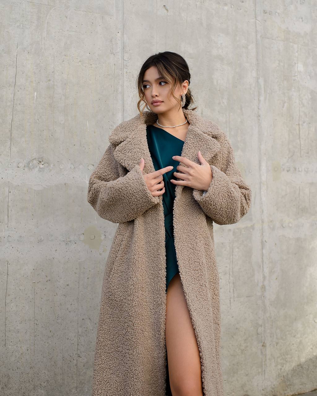 Woman wearing a long beige coat against a concrete wall