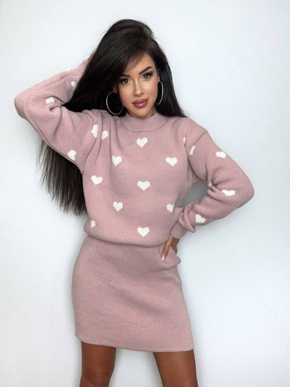 Woman wearing a pink sweater with heart patterns and matching skirt against a white background