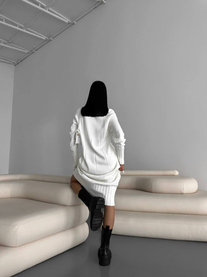 Person in a white outfit walking in a minimalistic room with gray walls and beige furniture.
