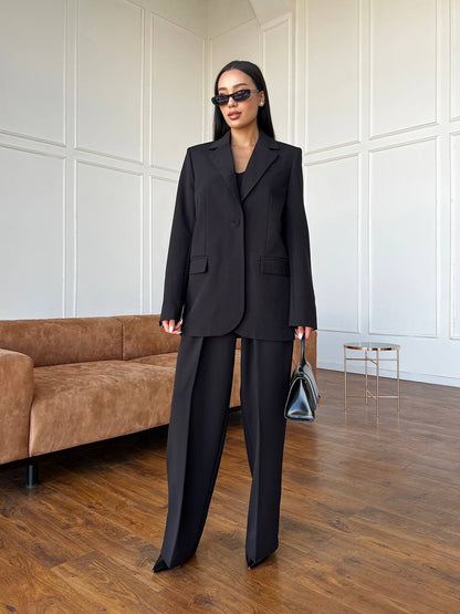 Woman in a black suit standing in a modern room with wooden flooring and a brown sofa.