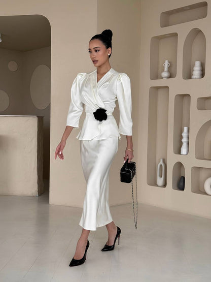 Woman in a white outfit with black details standing in a modern interior setting.