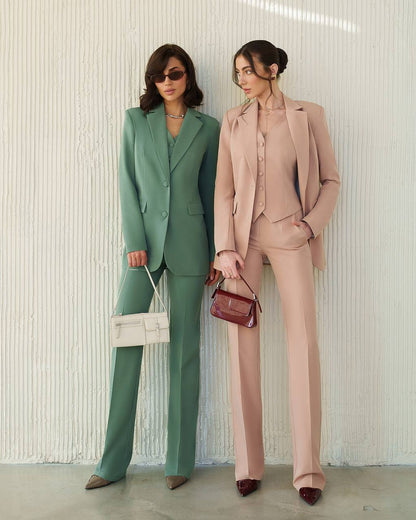 Two women in green and pink suits holding handbags against a neutral background