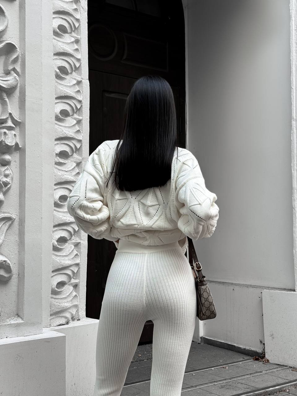 Person wearing a white outfit standing in front of a decorative wall.