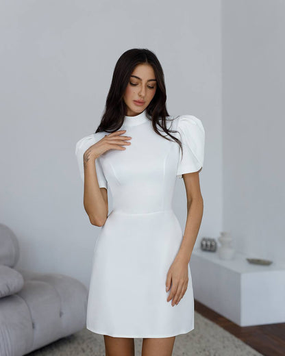 Woman wearing a white dress with puffed sleeves in a minimalistic room.