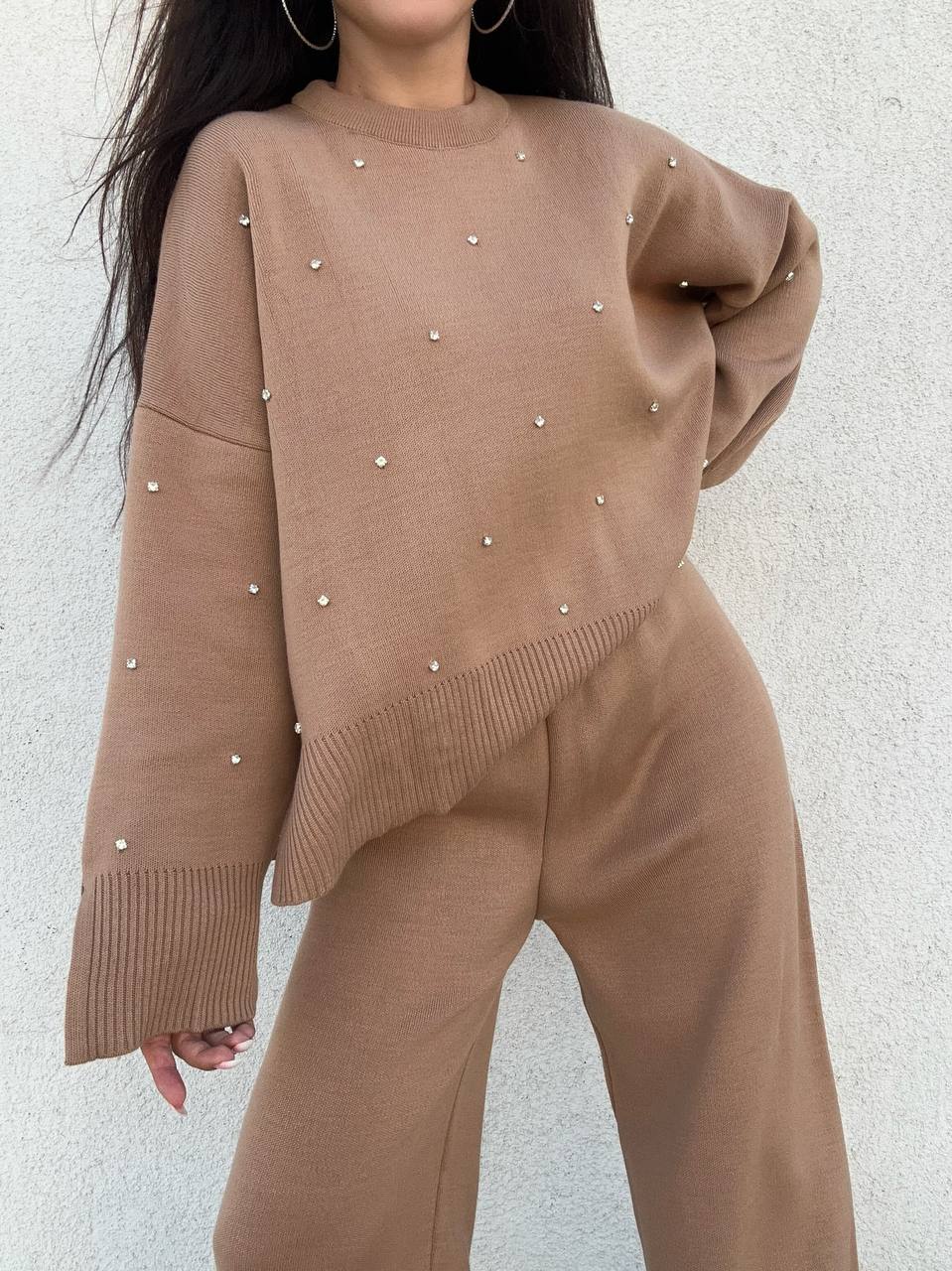 Brown sweater with pearl embellishments worn by a person against a light gray background