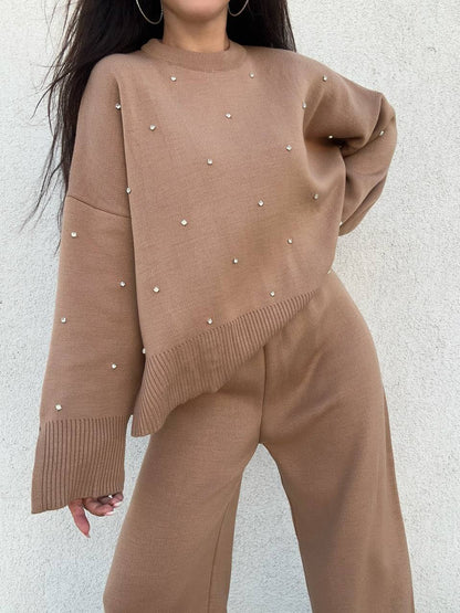 Brown sweater with pearl embellishments worn by a person against a light gray background