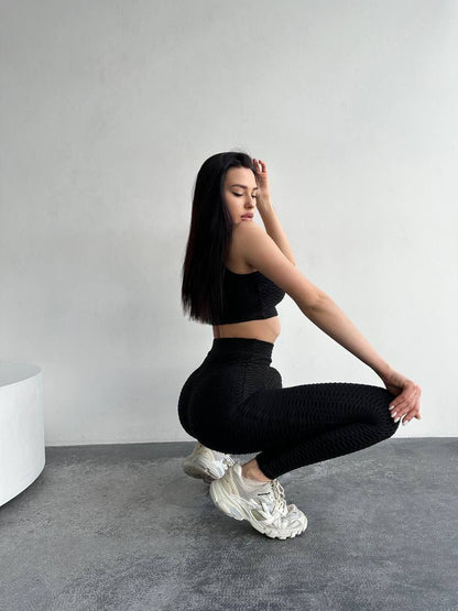 Woman in black athletic wear performing a squat against a plain background
