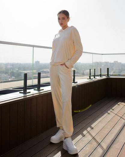 Person wearing a beige tracksuit standing on a rooftop with a cityscape view.