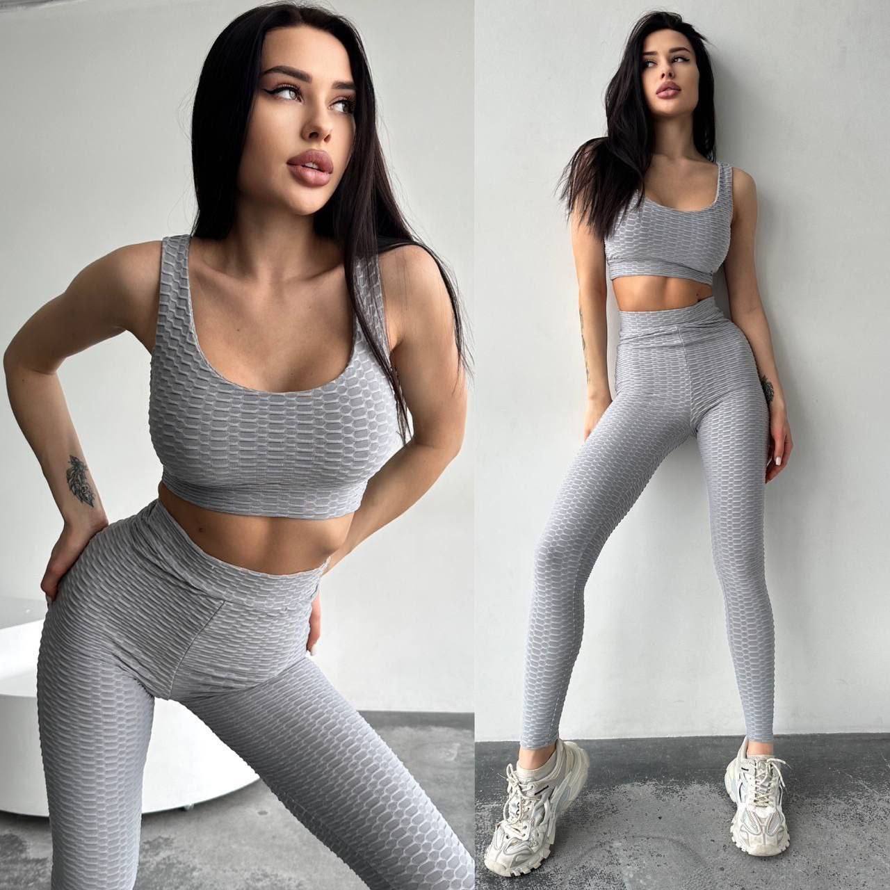 Woman wearing a gray athletic outfit posing against a plain background