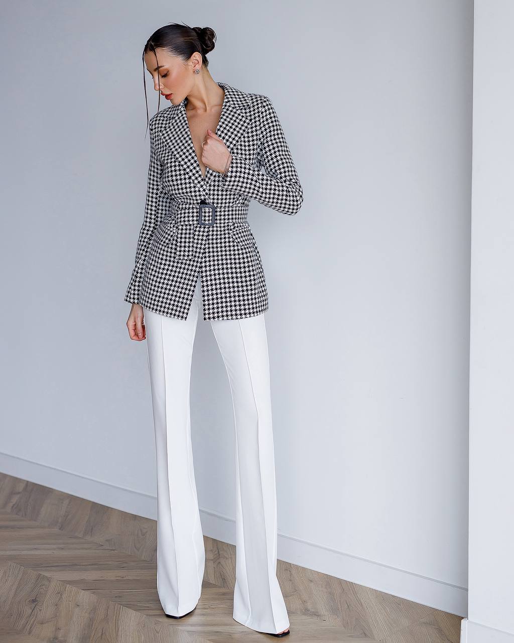 Woman wearing a checkered blazer and white pants against a plain background
