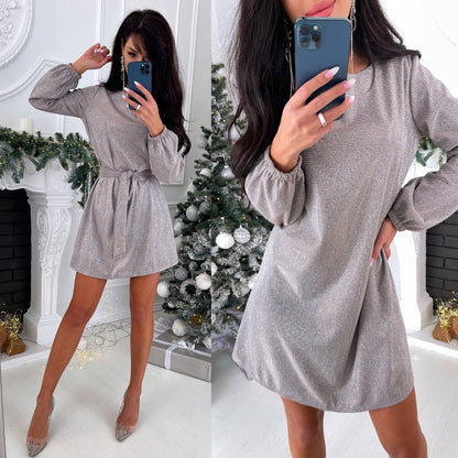 Woman in a gray dress taking a mirror selfie in a festive room with a Christmas tree.
