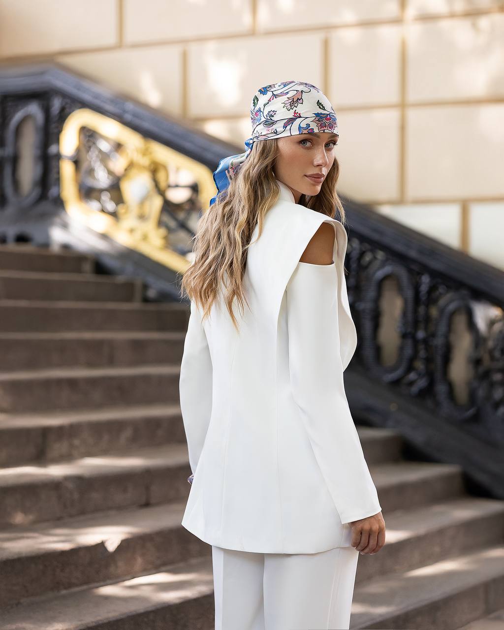 Woman in a white outfit with a patterned headscarf standing on steps.