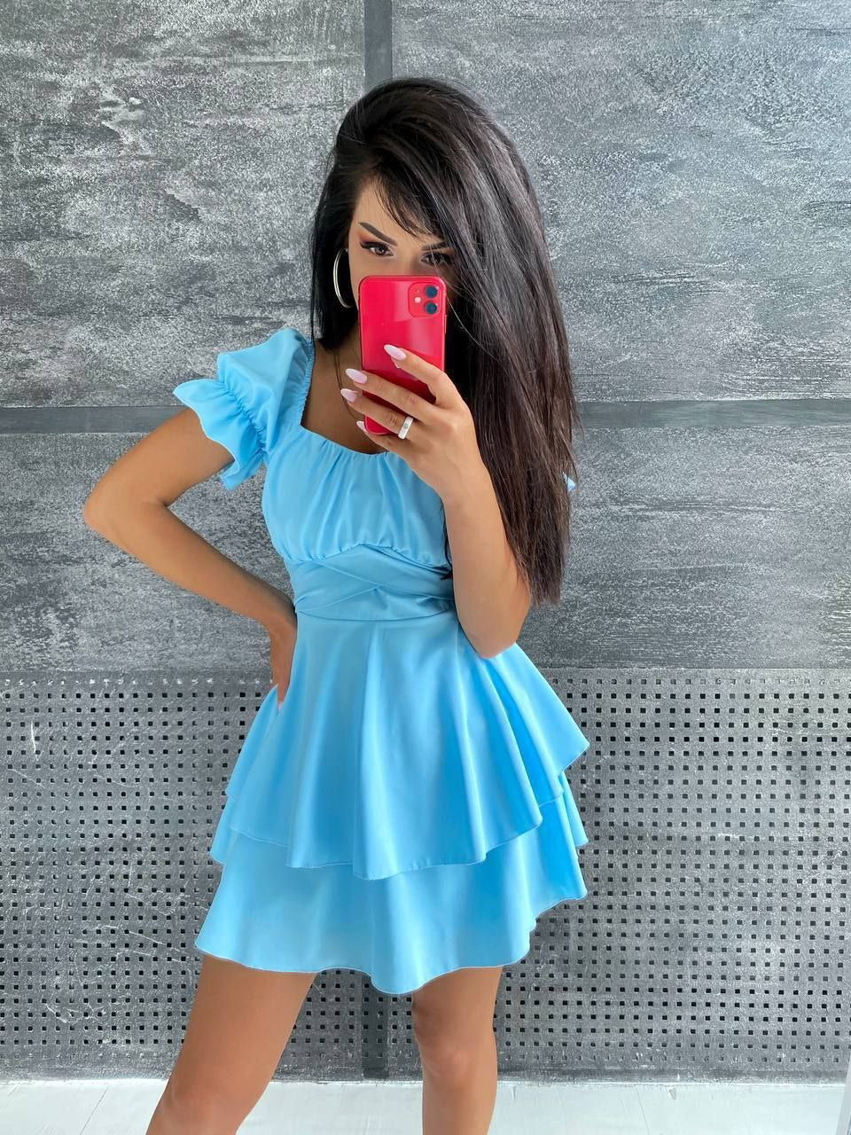 Woman taking a mirror selfie wearing a light blue dress against a gray textured wall.