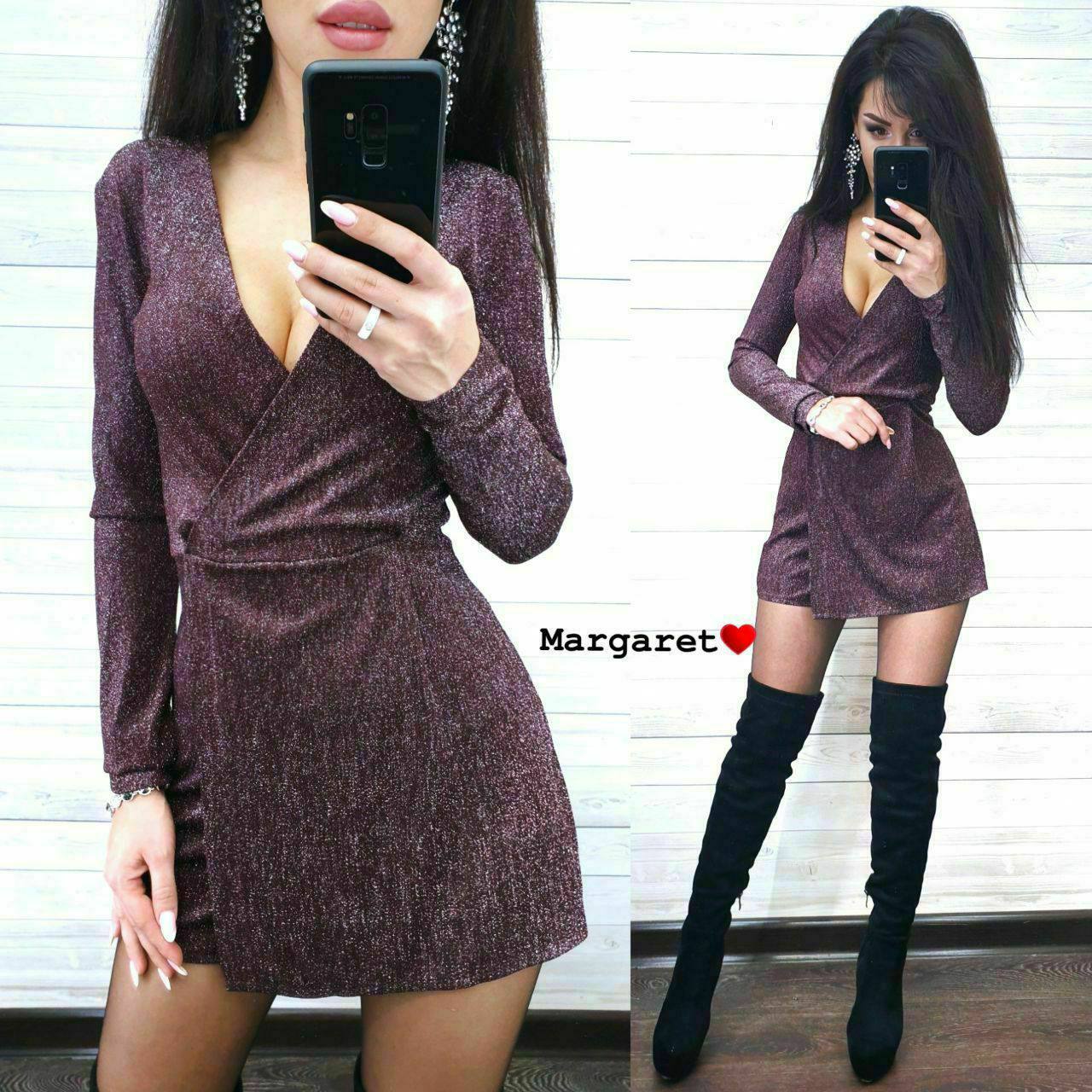 Woman wearing a sparkly purple dress and black knee-high boots, taking a mirror selfie.