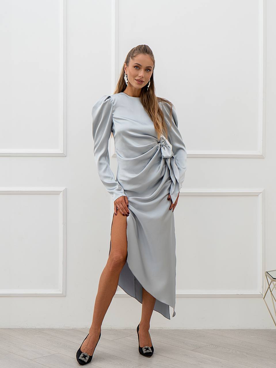 Woman wearing a light blue dress with long sleeves and a high slit in a white room.