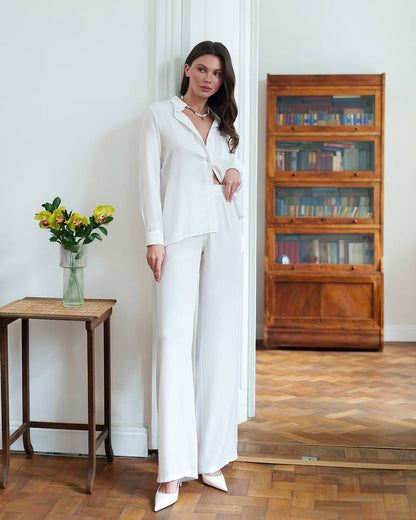Woman in a white outfit standing in a room with wooden flooring and a bookshelf.