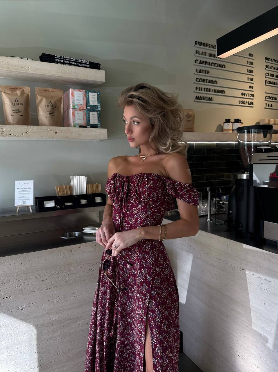 Woman in a floral dress standing in a coffee shop.