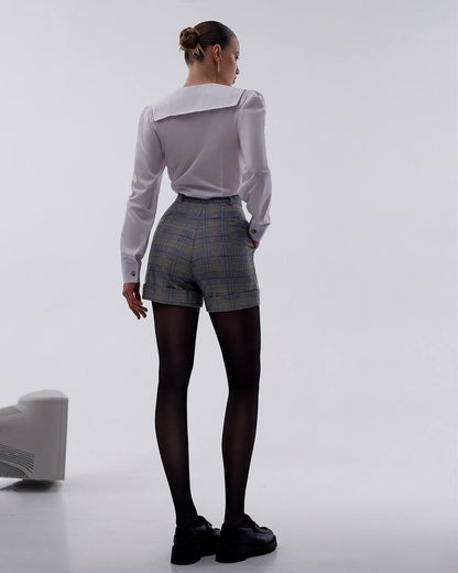 Person wearing a white blouse, plaid shorts, and black tights on a plain background
