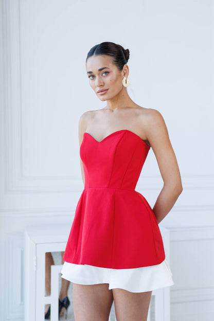 Woman wearing a red strapless dress with a white bottom half against a white background