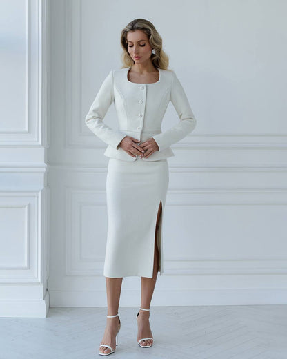 Woman wearing a white outfit with a jacket and skirt against a white wall.
