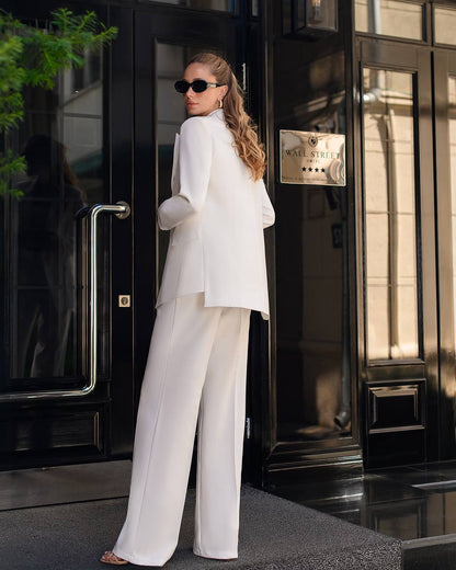 Woman in a white outfit standing outside a building with a sign.