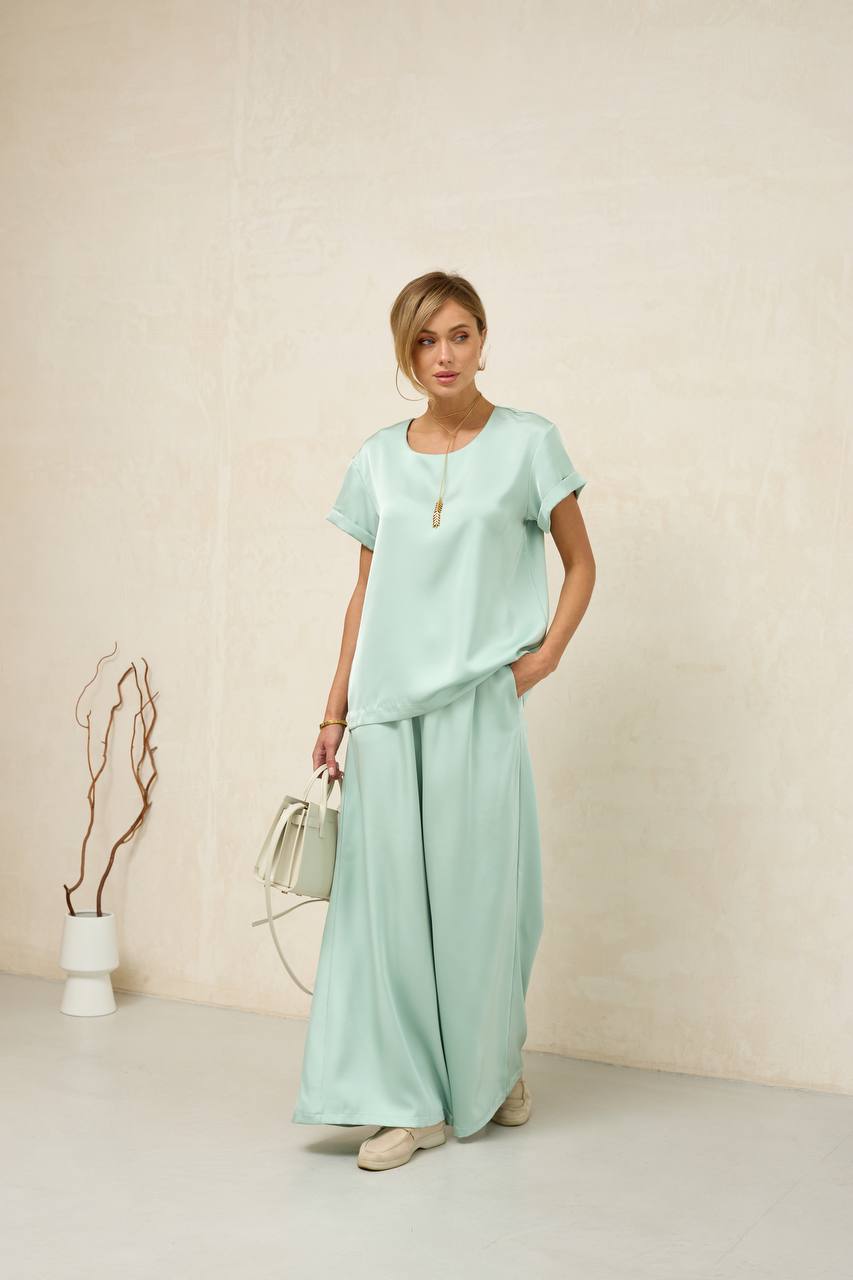Woman wearing a light green outfit with wide-leg pants against a plain background