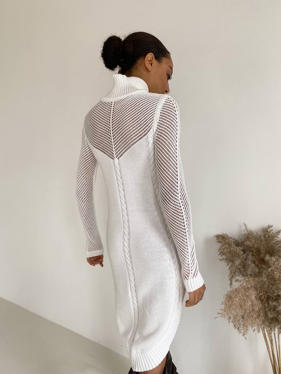 Woman wearing a white knit dress with open back against a plain background