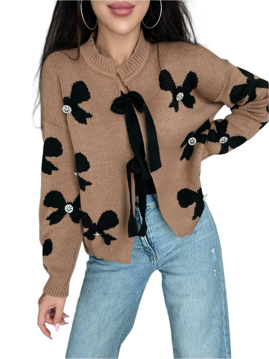 Beige sweater with black bow patterns worn by a person on a white background