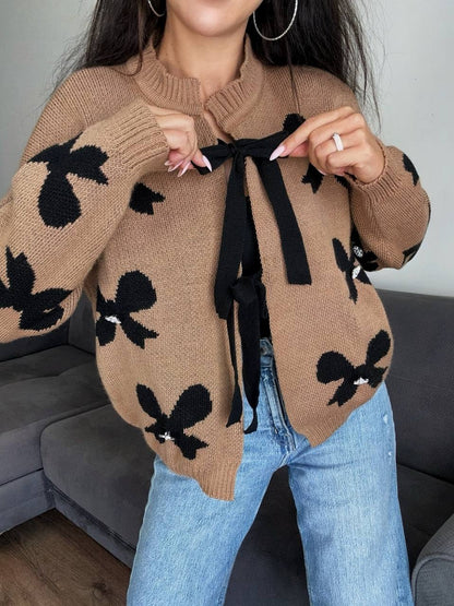 Person wearing a brown sweater with black bow patterns and blue jeans.