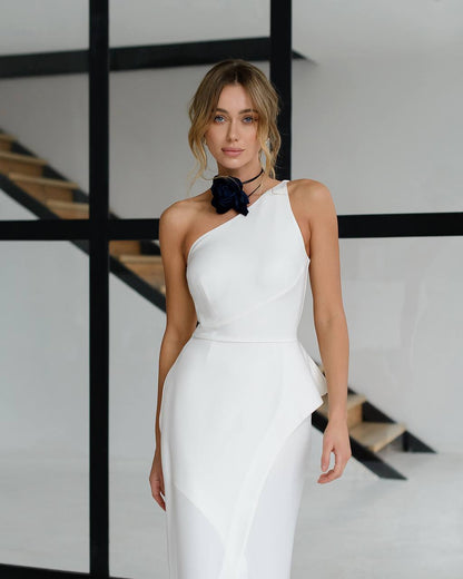 Woman in a white one-shoulder dress standing in a modern indoor setting.