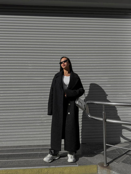 Person wearing a long black coat standing in front of a closed metal shutter.