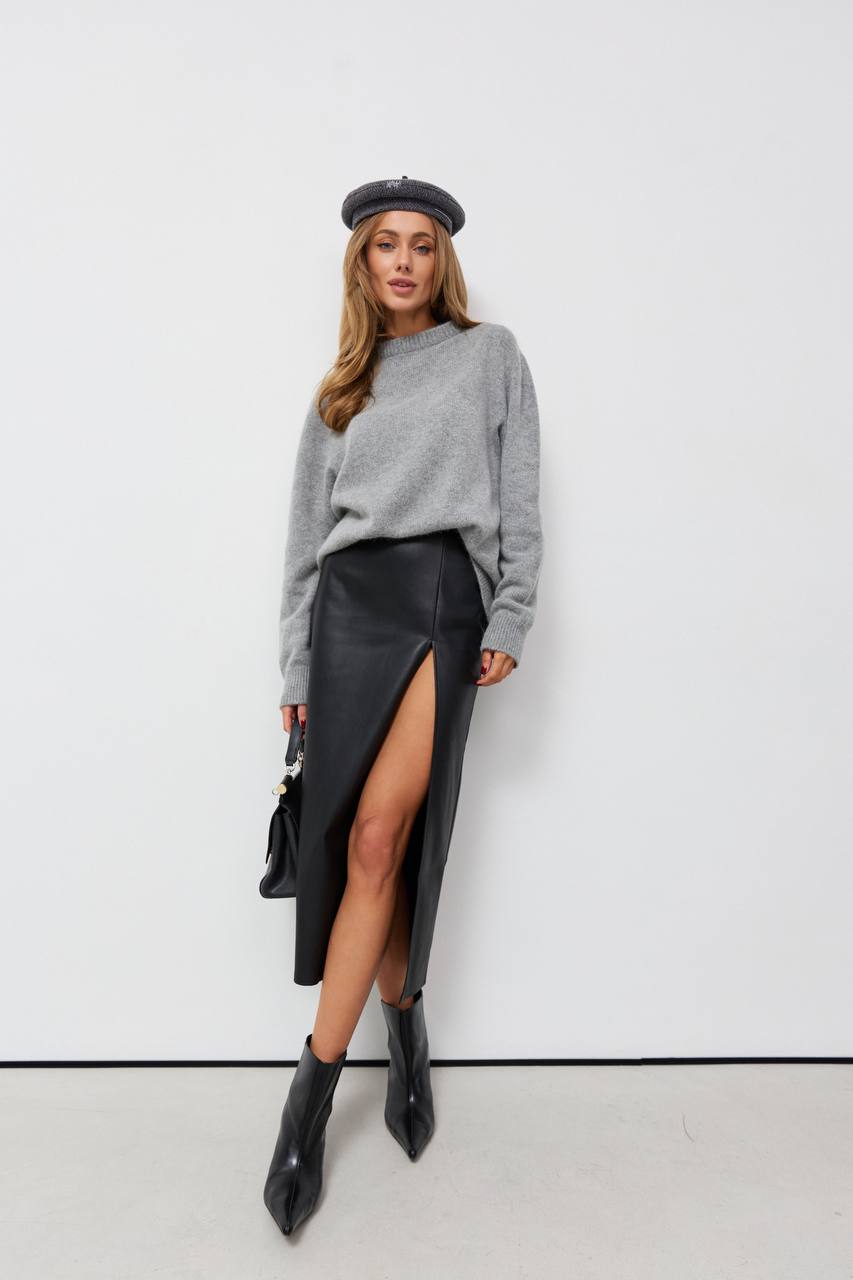Woman wearing a gray sweater, black leather skirt, and black boots against a white background