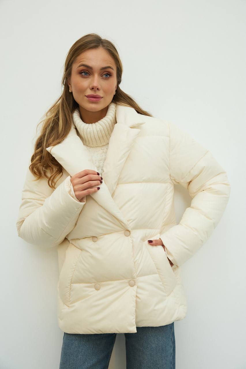 Woman wearing a cream puffer jacket against a white background