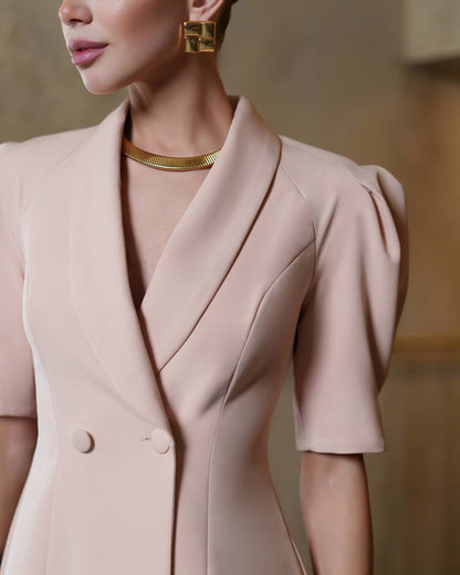 Close-up of a person wearing a light pink blazer with gold jewelry against a neutral background