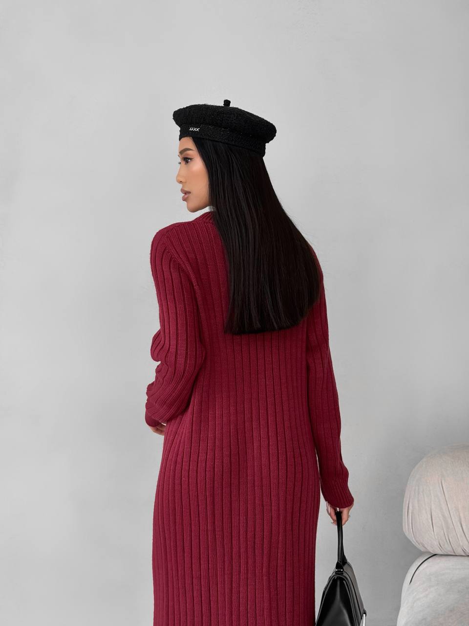Woman wearing a burgundy ribbed dress and black beret against a plain background